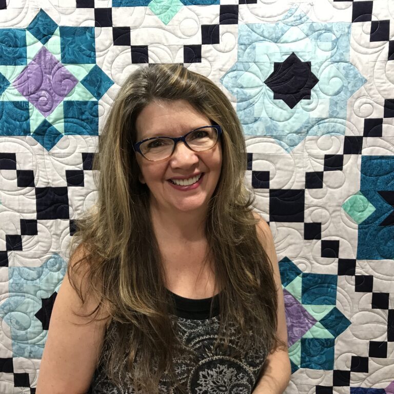 Paola Jo standing in front of beautiful E2E Hawthorn quilt done on a LongArm